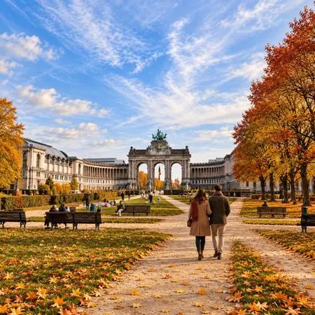 Couple walking along a tree-lined autumn park toward a grand archway in the distance.